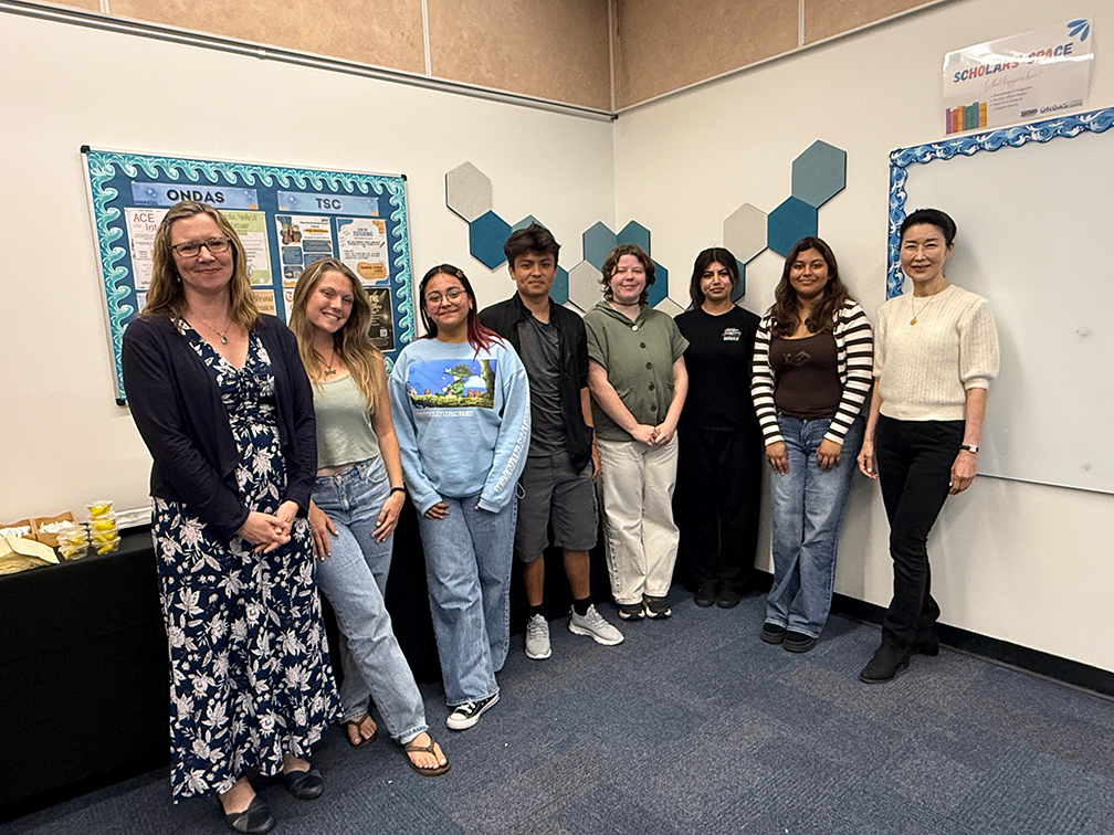 eight people in the faculty mentoring program standing in the corner of a room